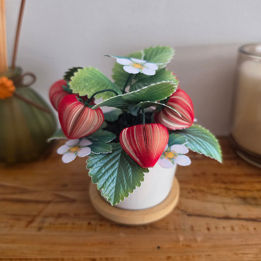 Strawberry Plant Pot on a wooden shelf with a diffuser and candle, handmade book-art strawberries with printed card leaves