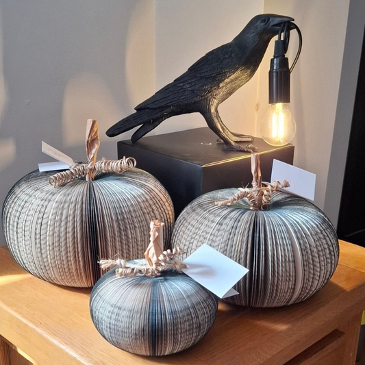 Decorative pumpkins with a crow sculpture and light bulb on a wooden surface.