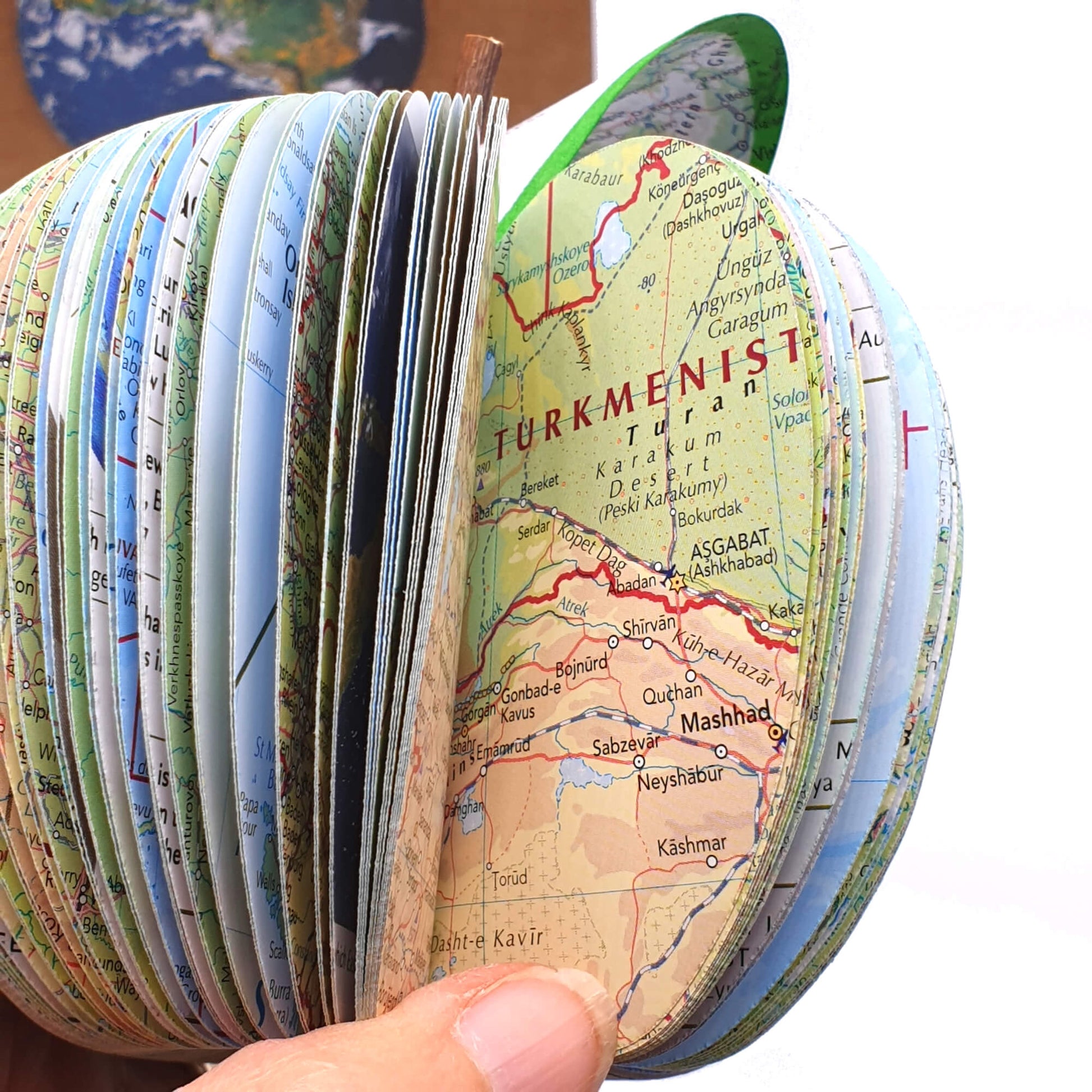 Close-up inside view of a handmade map apple crafted from real world atlas pages, showing detailed country maps and layered paper design