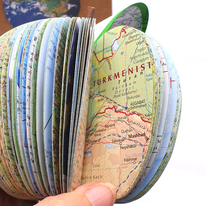 Close-up inside view of a handmade map apple crafted from real world atlas pages, showing detailed country maps and layered paper design