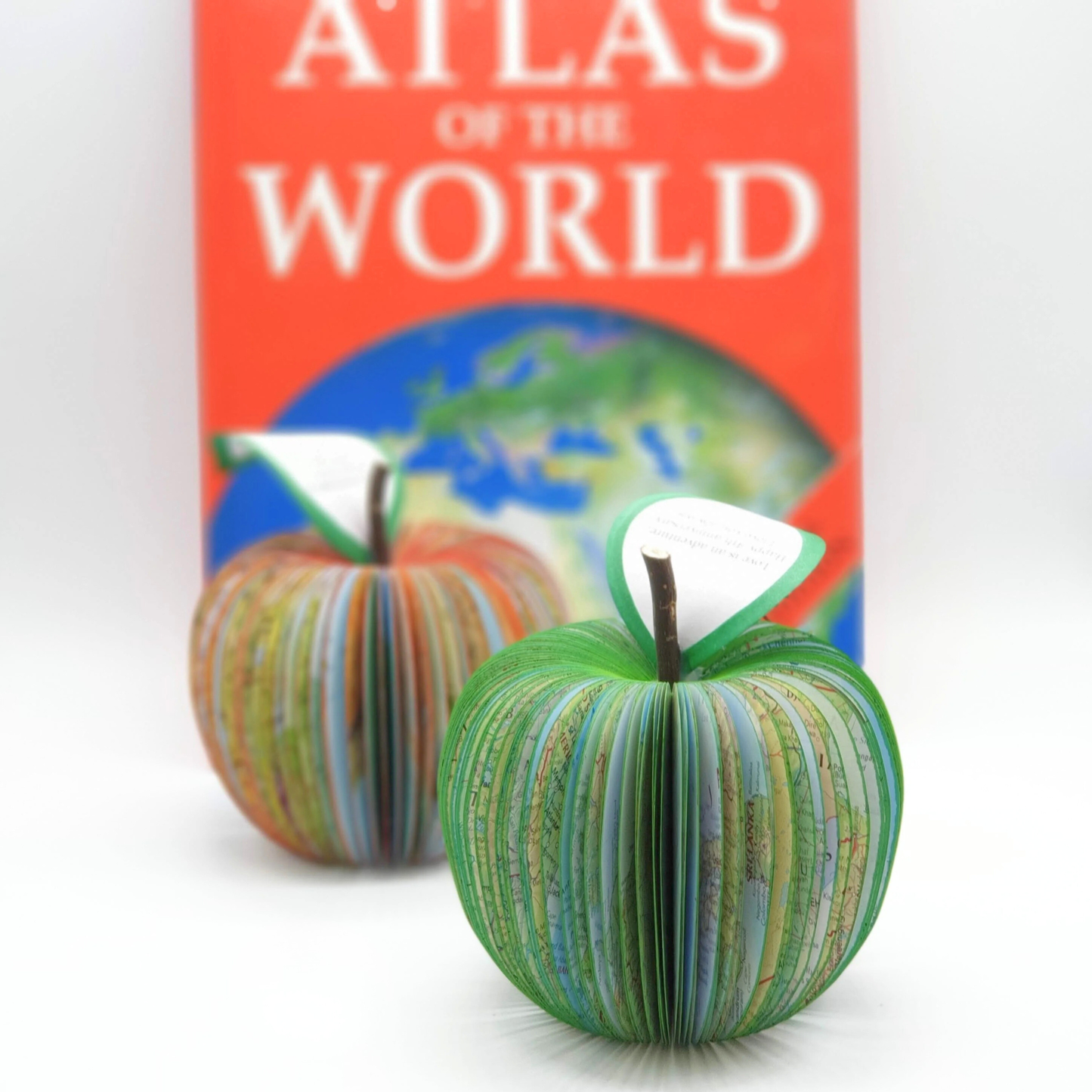 Map apple handmade from real world atlas pages displayed beside original atlas book