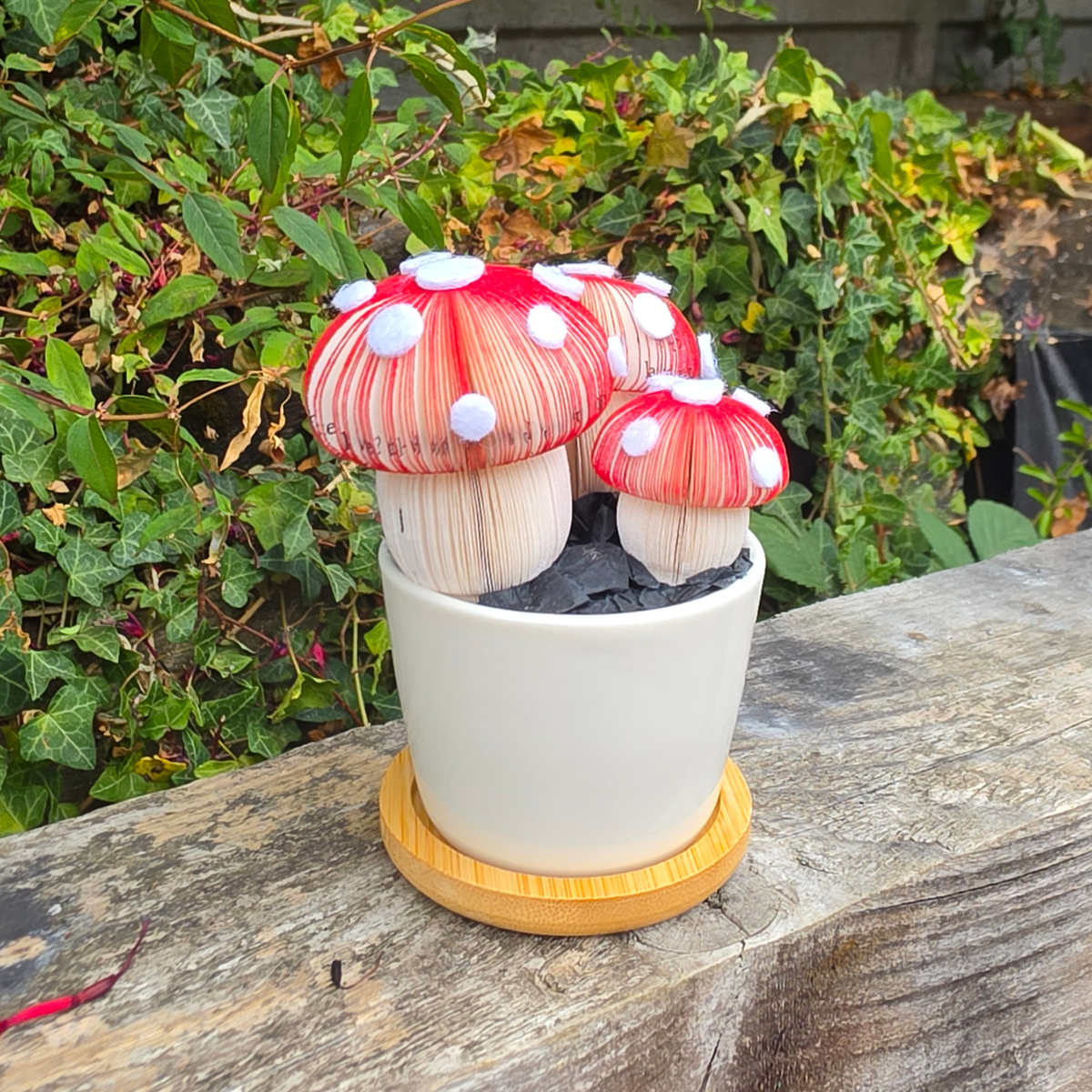 Close-up of handmade toadstool mushrooms hand-cut from book pages, Toadstool Trio Pot displayed outdoors on a wooden fence