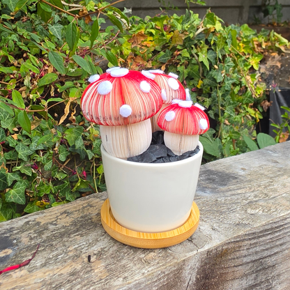 Close-up of handmade toadstool mushrooms hand-cut from book pages, Toadstool Trio Pot displayed outdoors on a wooden fence
