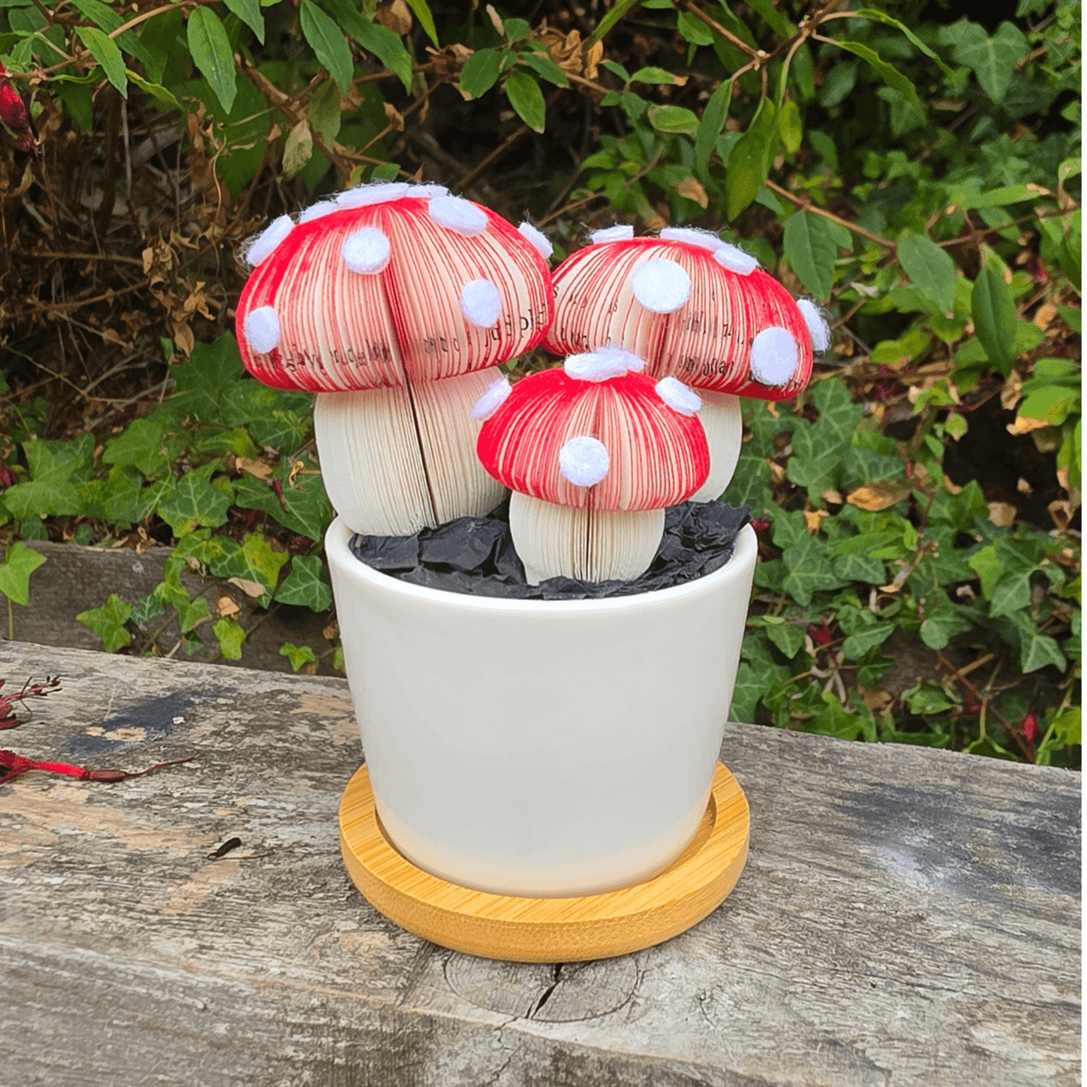 Toadstool Trio Pot, three handmade red and white spotted toadstools hand-cut from book pages in a white ceramic pot outdoors