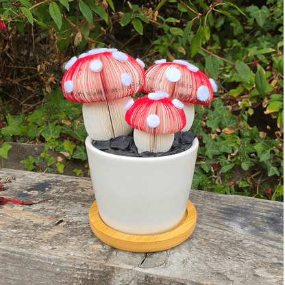 Toadstool Trio Pot, three handmade red and white spotted toadstools hand-cut from book pages in a white ceramic pot outdoors